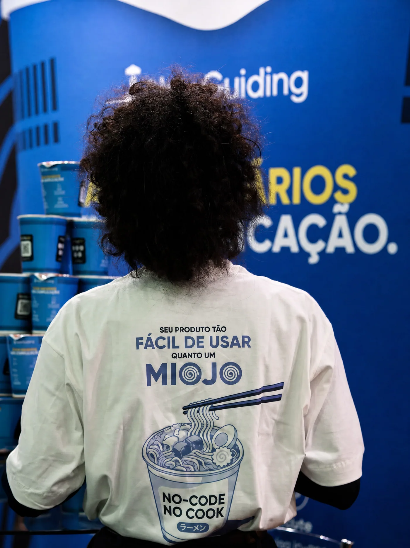 Integrante da equipe usando a camiseta diante do estande da UserGuiding