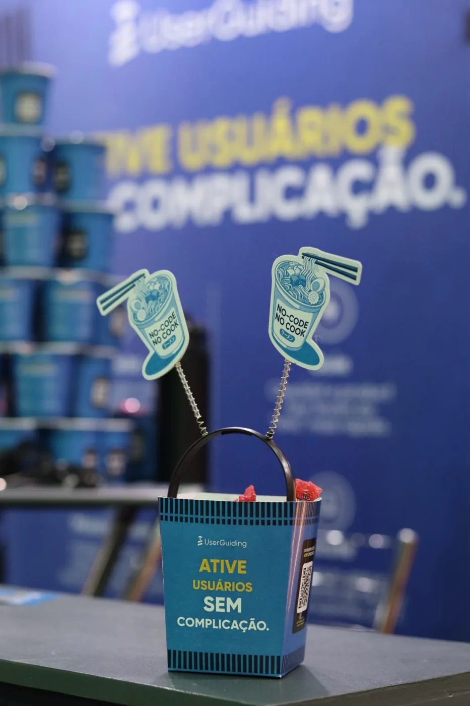 Tiara com o copo de miojo em mola, diante do painel